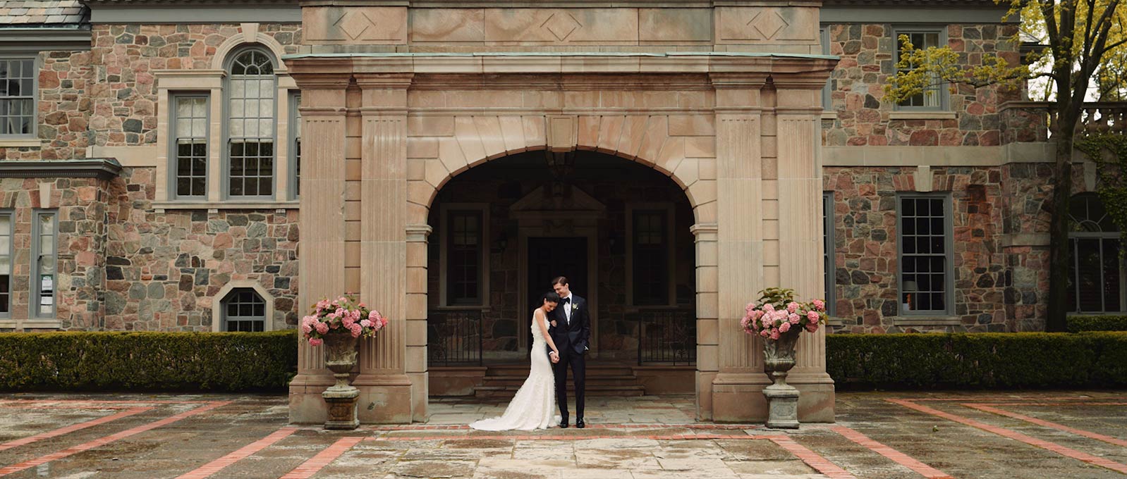 A bride and groom stand in front of Graydon Hall Manor by Outside In Studio, Toronto Wedding Videographers