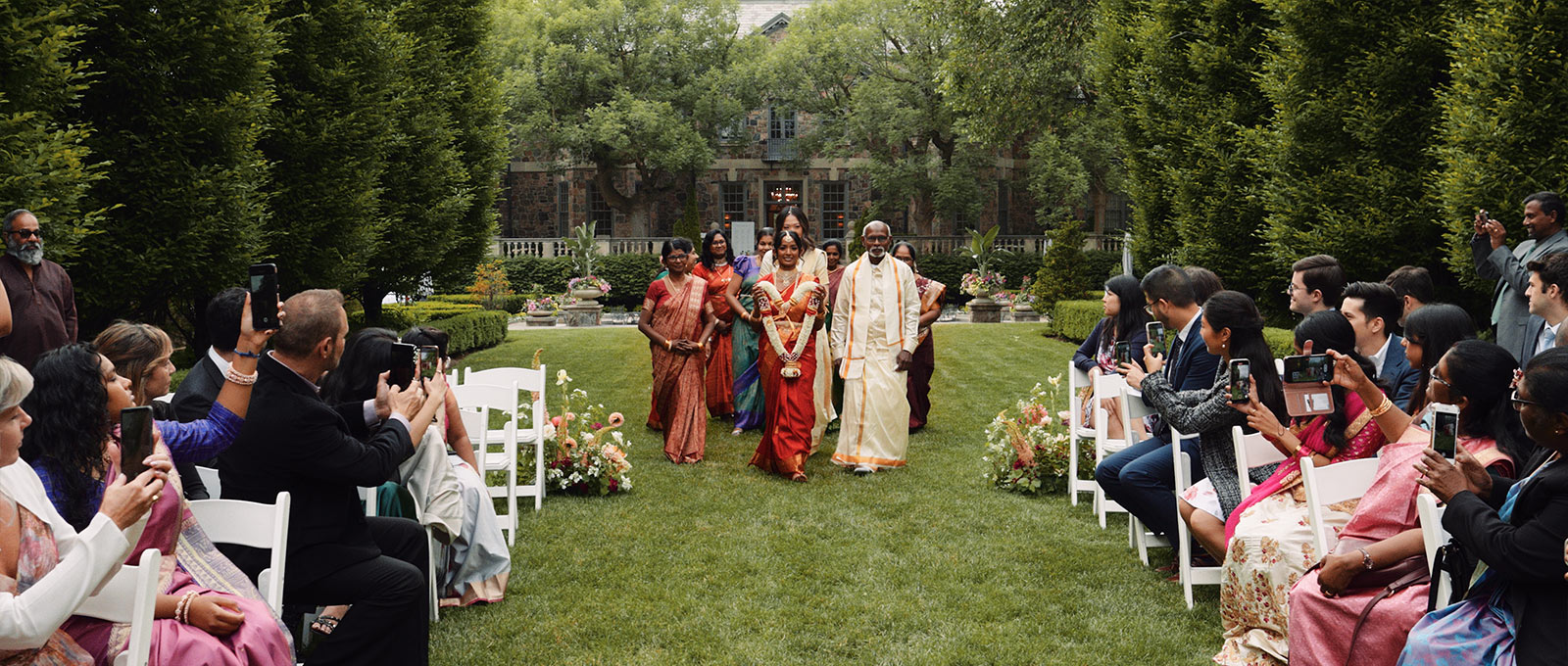 Hindu bride walks down the aisle with her family during a garden wedding ceremony at Graydon Hall Manor.